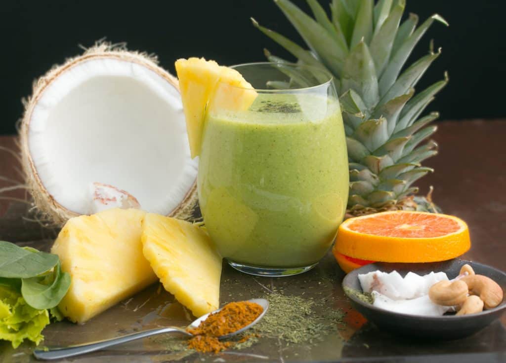 green pineapple coconut water smoothie in glass with ingredients surrounding