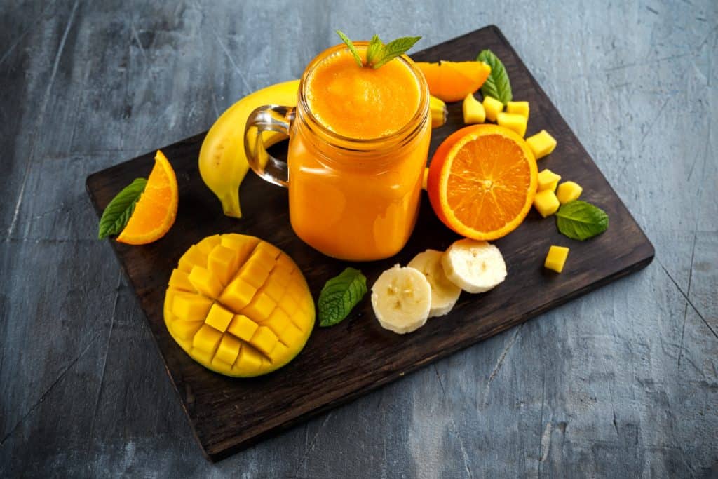 mango orange smoothie in glass on cutting board with ingredients surrounding