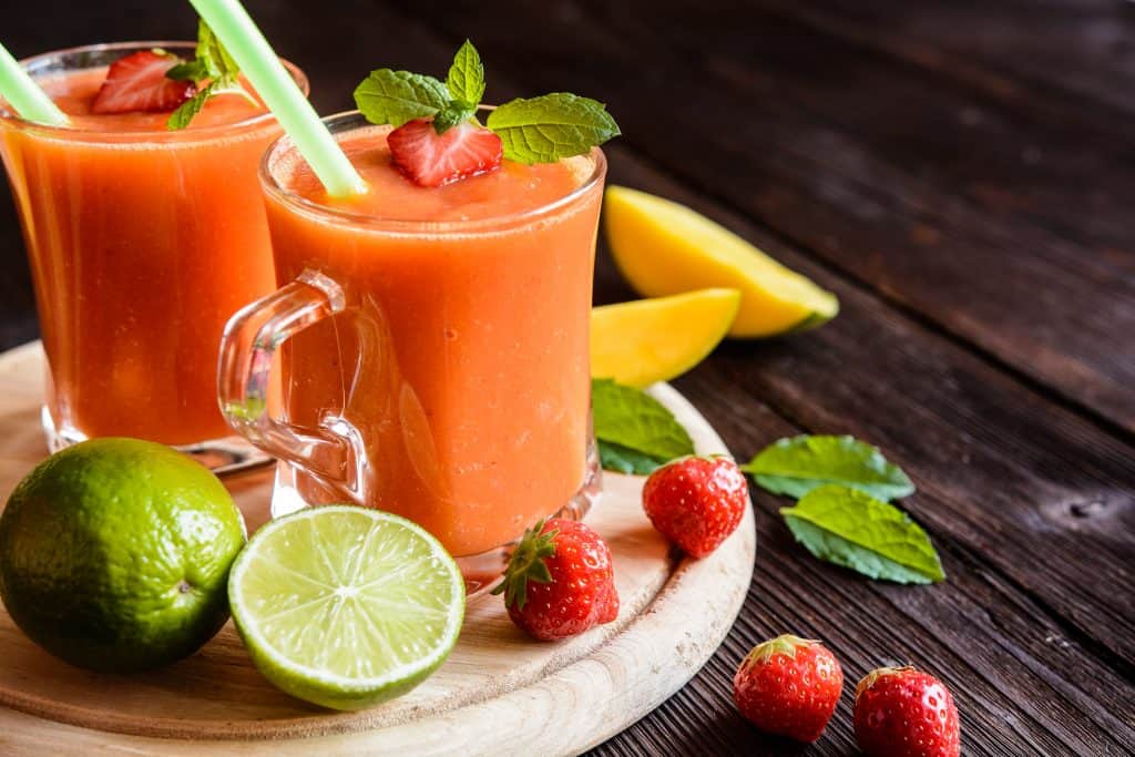smoothies made with water, strawberries, mango and lime juice in glasses with ingredients surrounding