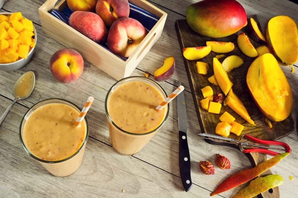 overhead view of fresh coconut oil smoothies with peaches and mango in background