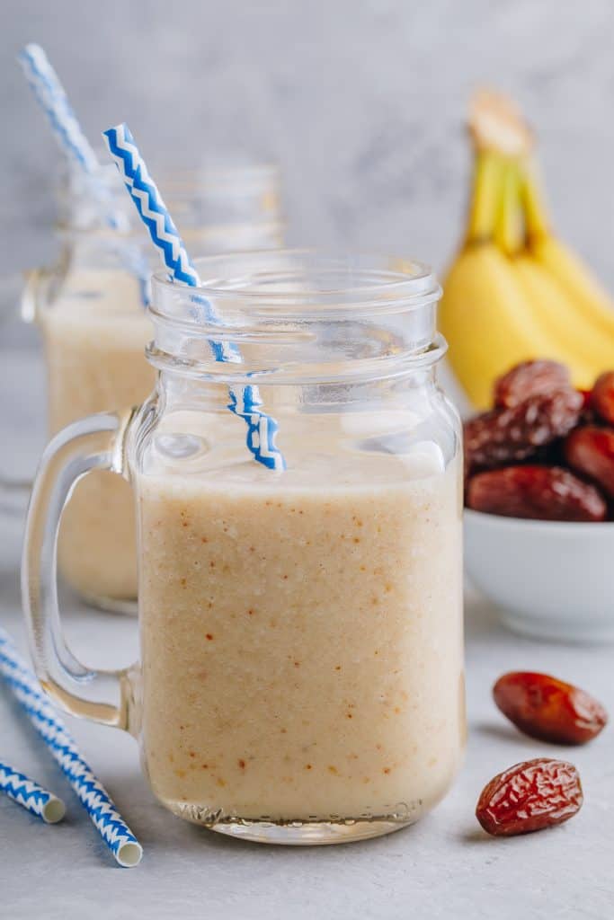 Banana and date fruit smoothie in glass mason jar on a grey stone background