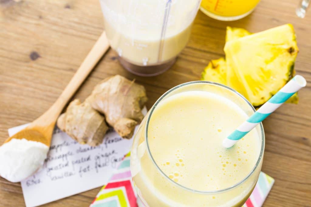ginger pineapple smoothie in glass with fresh ginger and pineapple in background