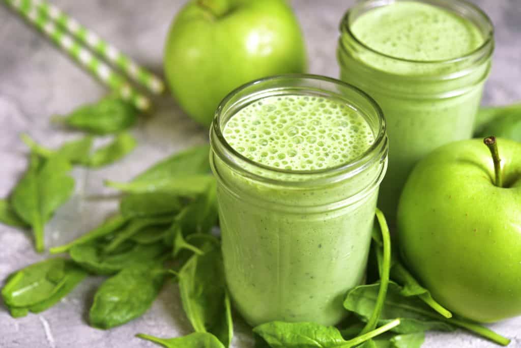 sour apple smoothie in glasses with green apples and spinach surrounding