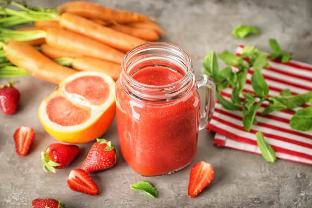 strawberry carrot smoothie in glass with ingredients surrounding
