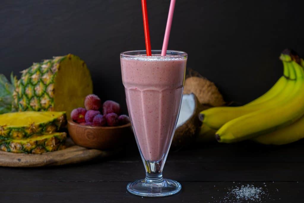 strawberry colada smoothie in glass with ingredients in background