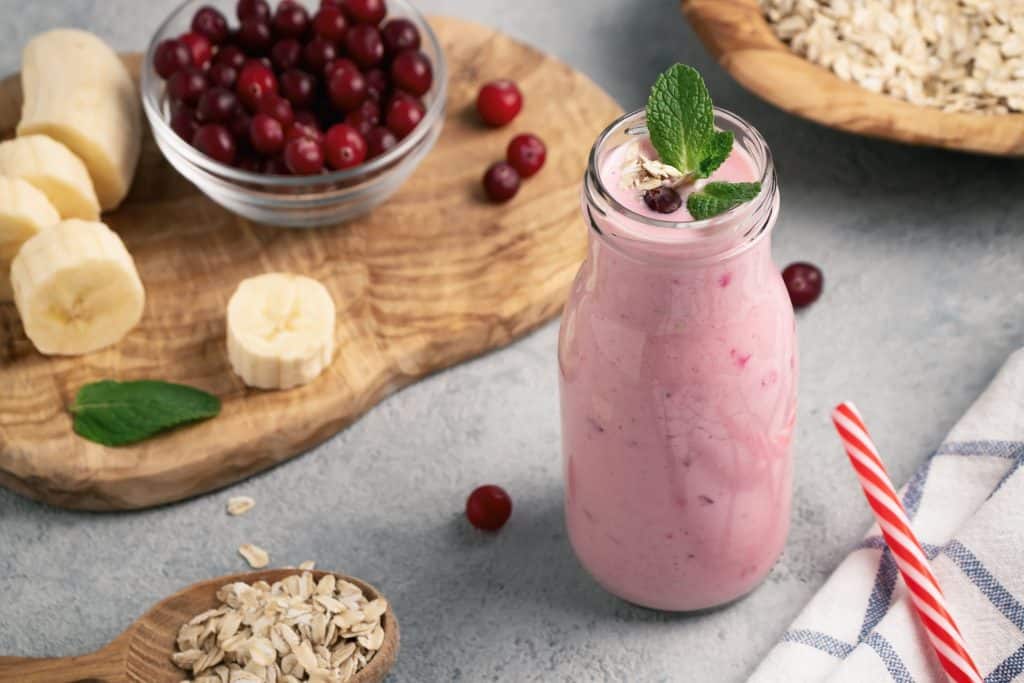 triple berry oat smoothie in tall glass with ingredients surrounding
