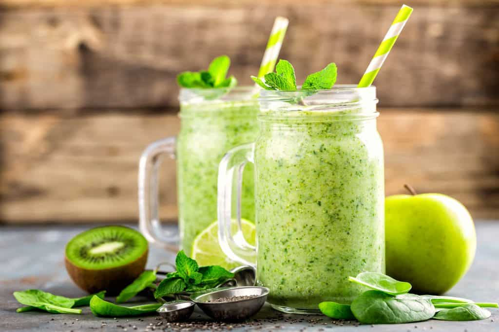 kiwi smoothie without banana in two glass jars with ingredients surrounding