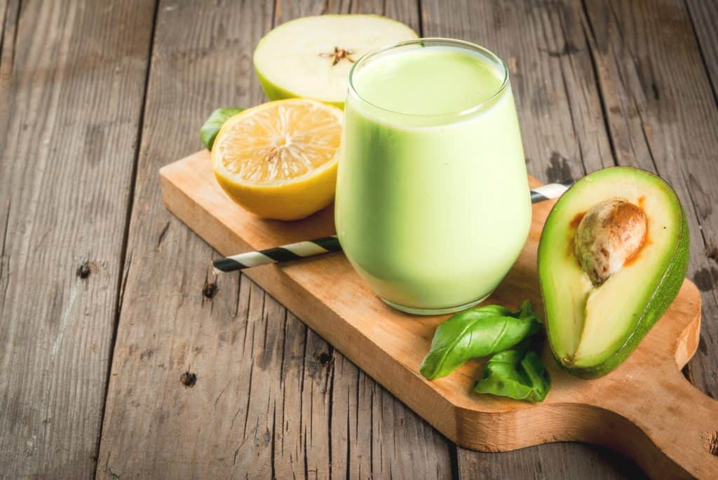 Green smoothie made from avocado, banana, apple, spinach and lemon. On a rustic wooden table, with ingredients.