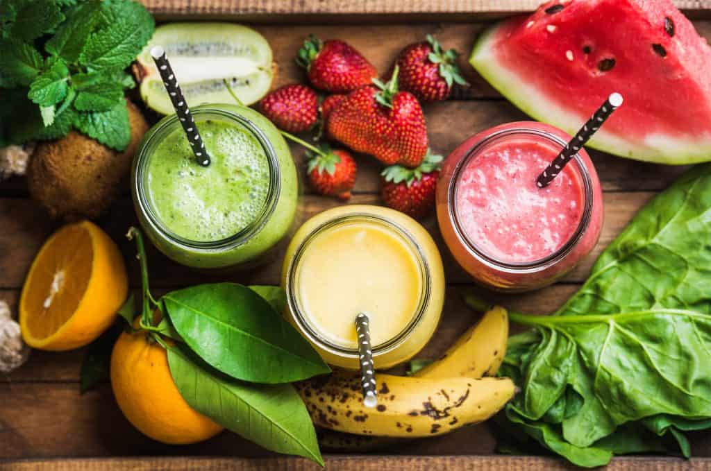 assortment of fruit and veggie smoothies on wooden table with fresh produce surrounding