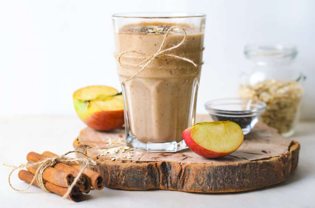 apple cinnamon oats smoothie in glass with apple, cinnamon and oats in background