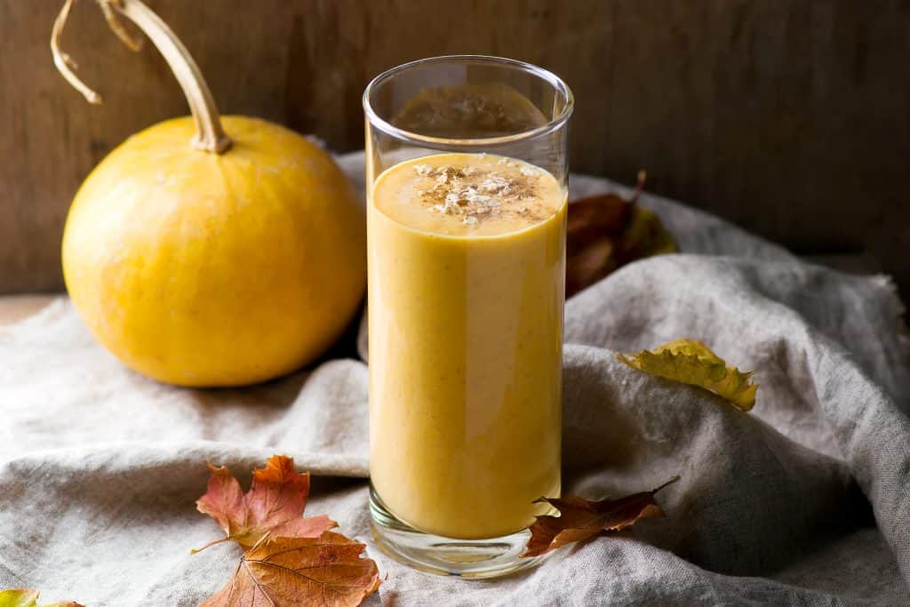 glass of pumpkin oatmeal smoothie with leaves and pumpkin in background