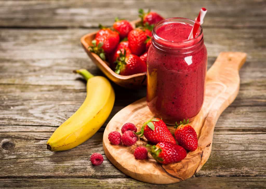 berry banana psyllium husk smoothie on wooden table with fruit surrounding