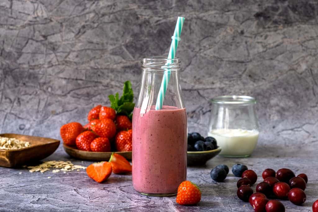 fresh strawberry blueberry smoothie in glass with ingredients in background