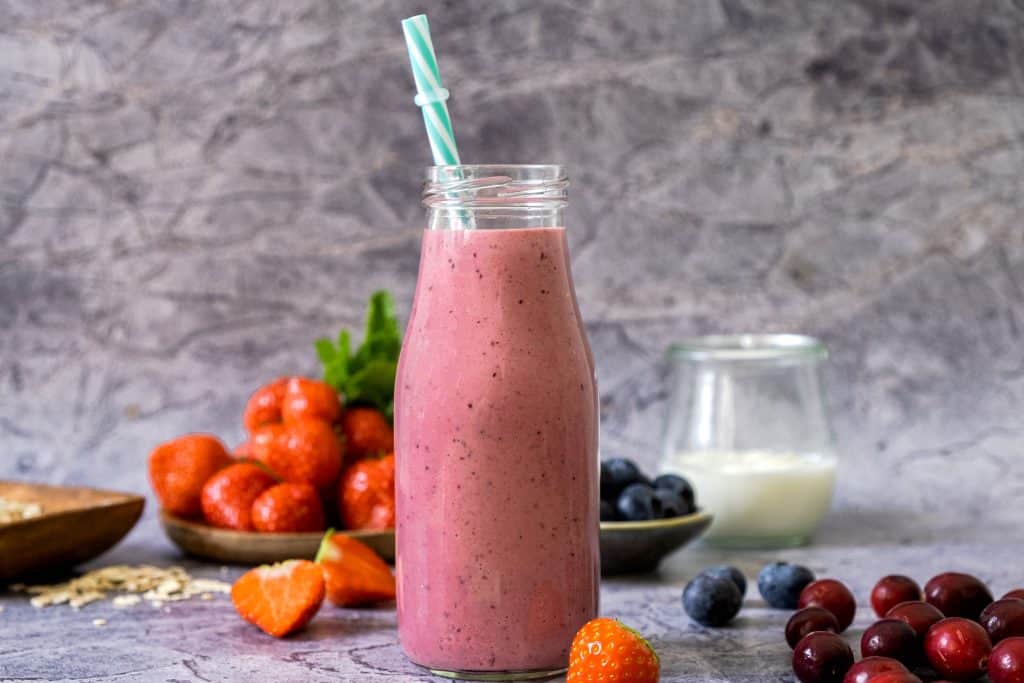strawberry blueberry smoothie in glass with fruit in background