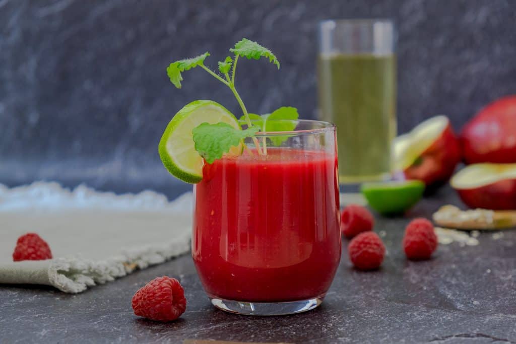 apple raspberry smoothie in glass with ingredients in background