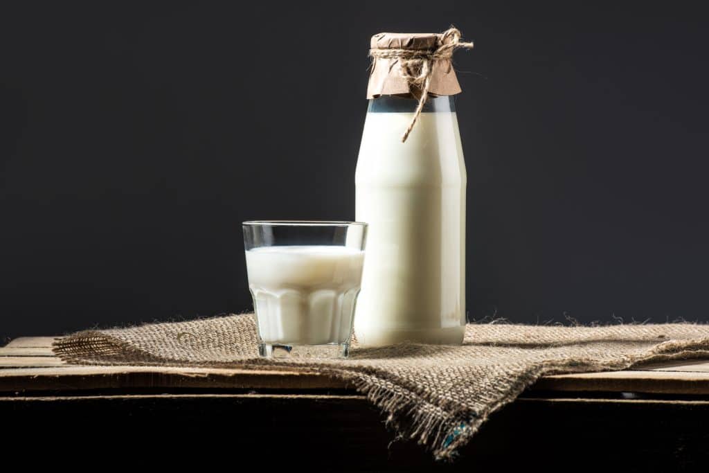 glass of milk or cream with bottle on dark background