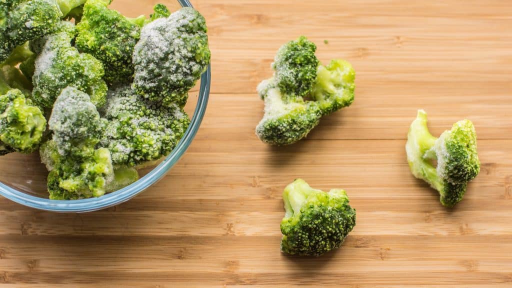 frozen broccoli in bowl on wooden background