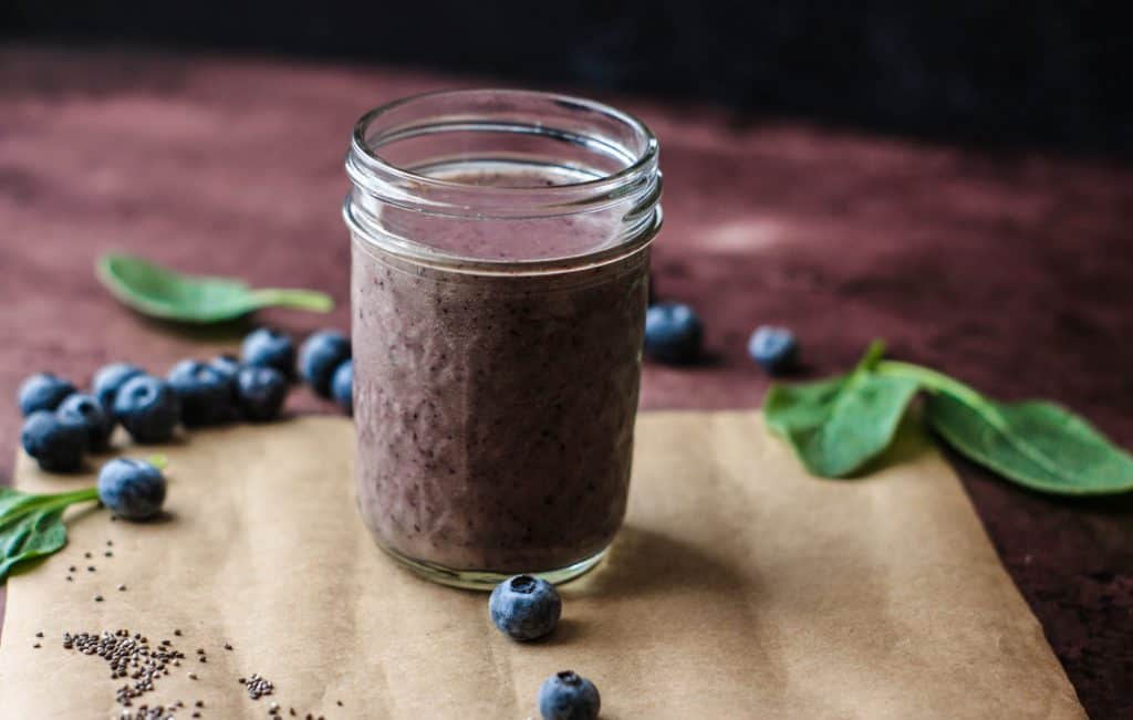 paleo blueberry smoothie in glass with blueberries and spinach surrounding
