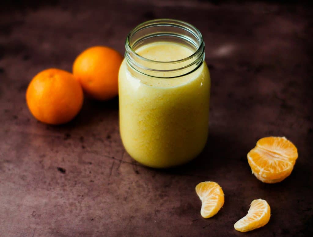 orange detox smoothie in glass with oranges surrounding