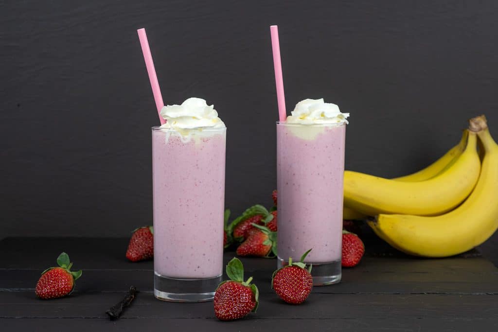 strawberry banana smoothies with ice cream with strawberries and bananas in background