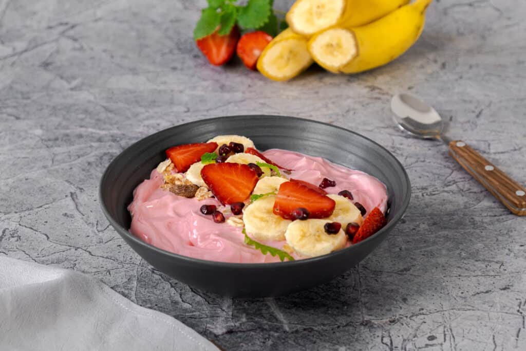 strawberry banana smoothie bowl on counter with spoon and fruit