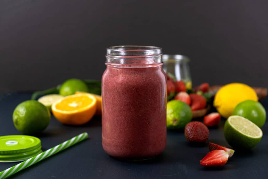 strawberry chia lemonade smoothie in glass with ingredients behind smoothie