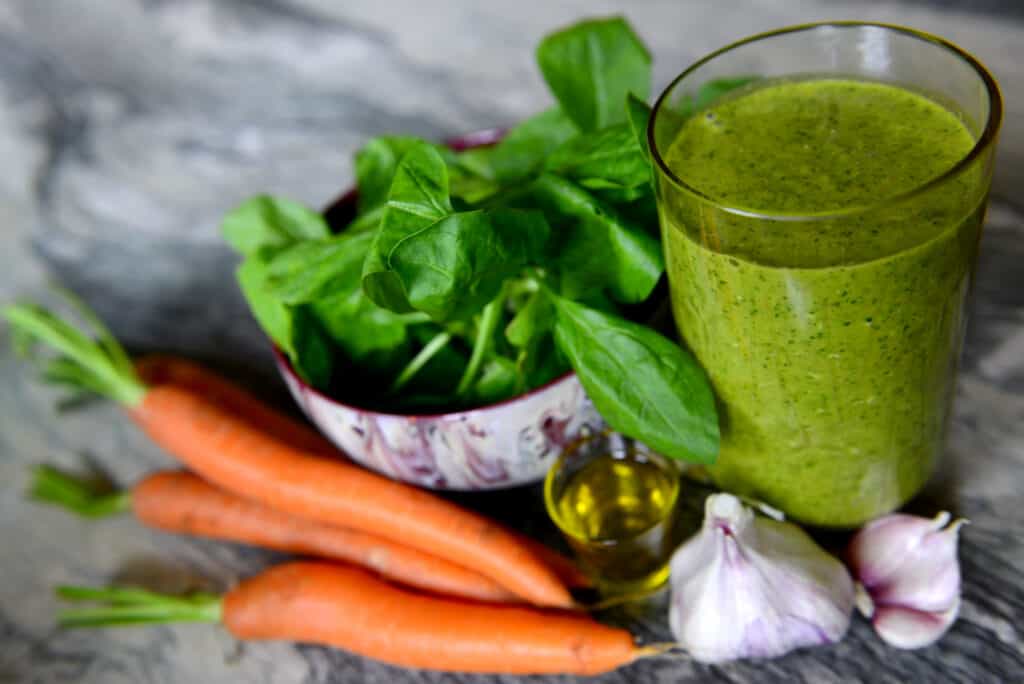 green smoothie in glass with carrots, garlic, and greens