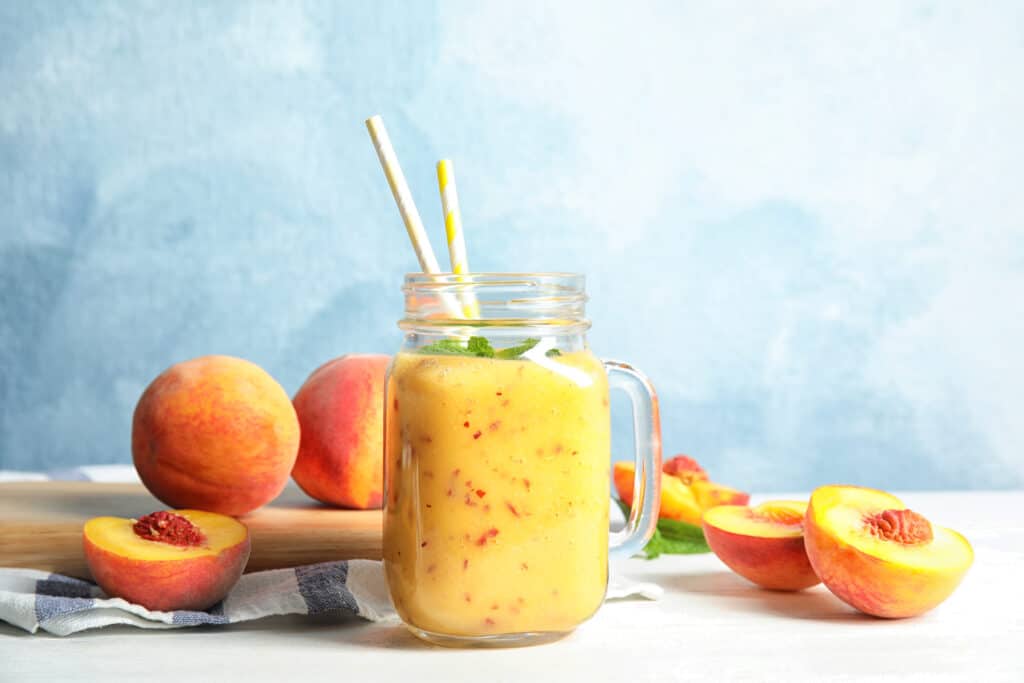 low carb peach smoothie in glass with peaches in background