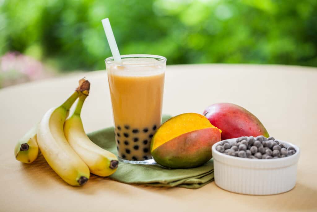 mango smoothie with boba in glass with ingredients surrounding