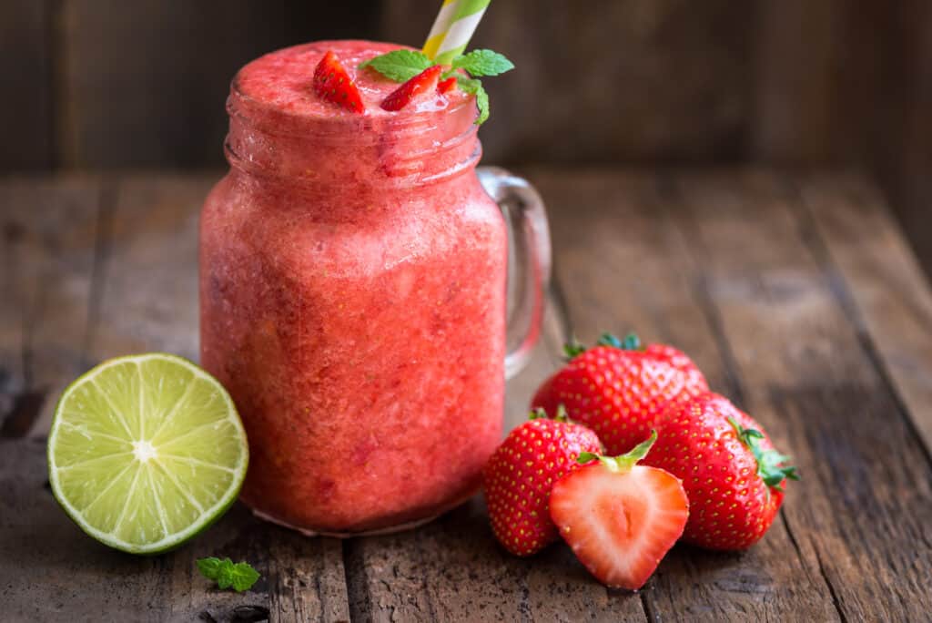 strawberry lime smoothie in glass with straw.  strawberries and lime in background
