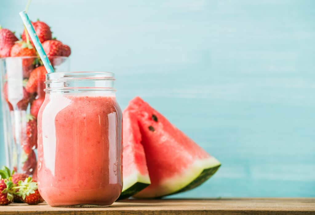 delicious watermelon protein smoothie on table with watermelon and strawberries in background