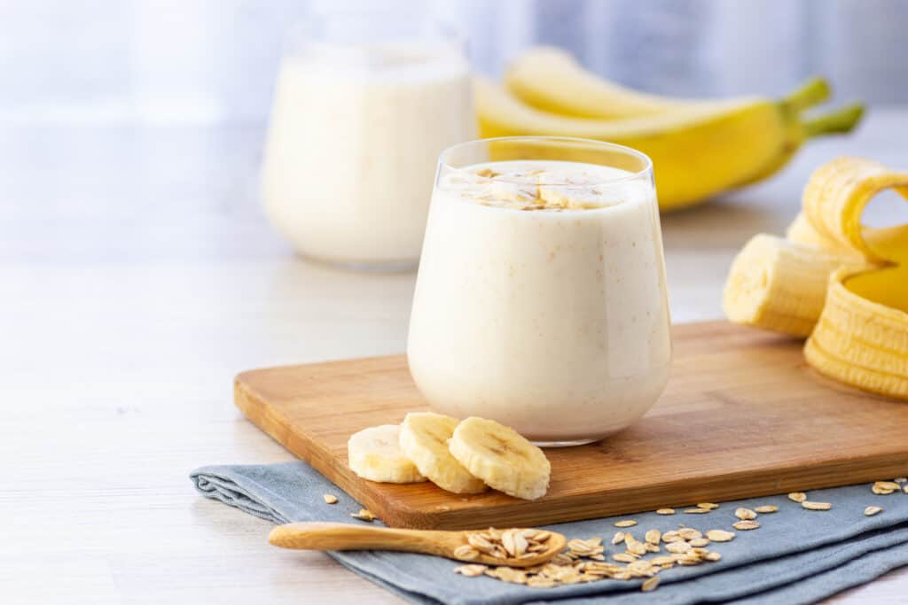 vegan banana, oat and slmond milk smoothie in glass with ingredients behind