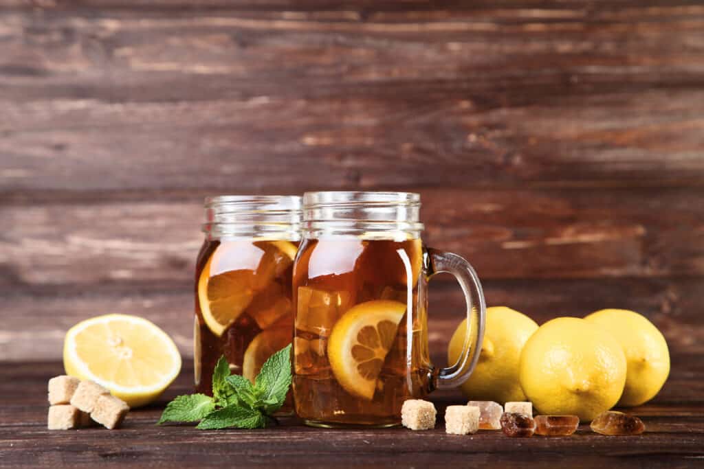 Ice tea in glass jars with lemon and mint leafs on wooden table