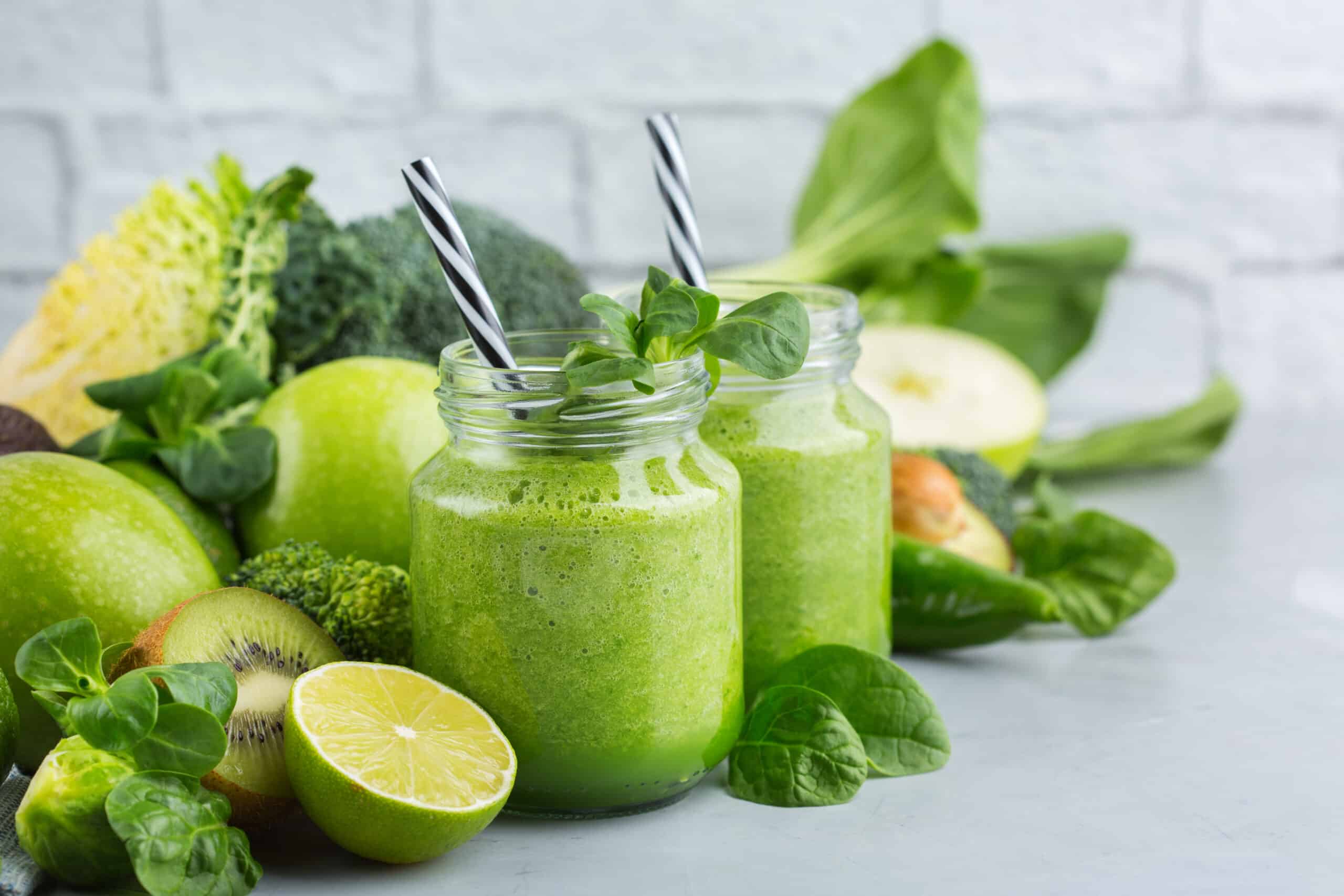 two green smoothies with straws and healthy green ingredients