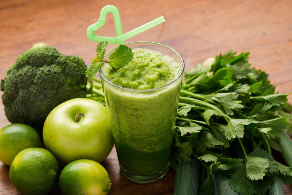 a foamy green smoothie with ingredients surrounding
