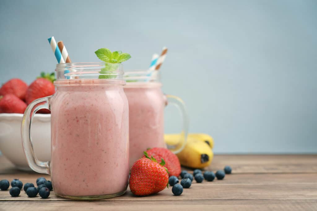 strawberry banana blueberry smoothie in glasses with ingredients