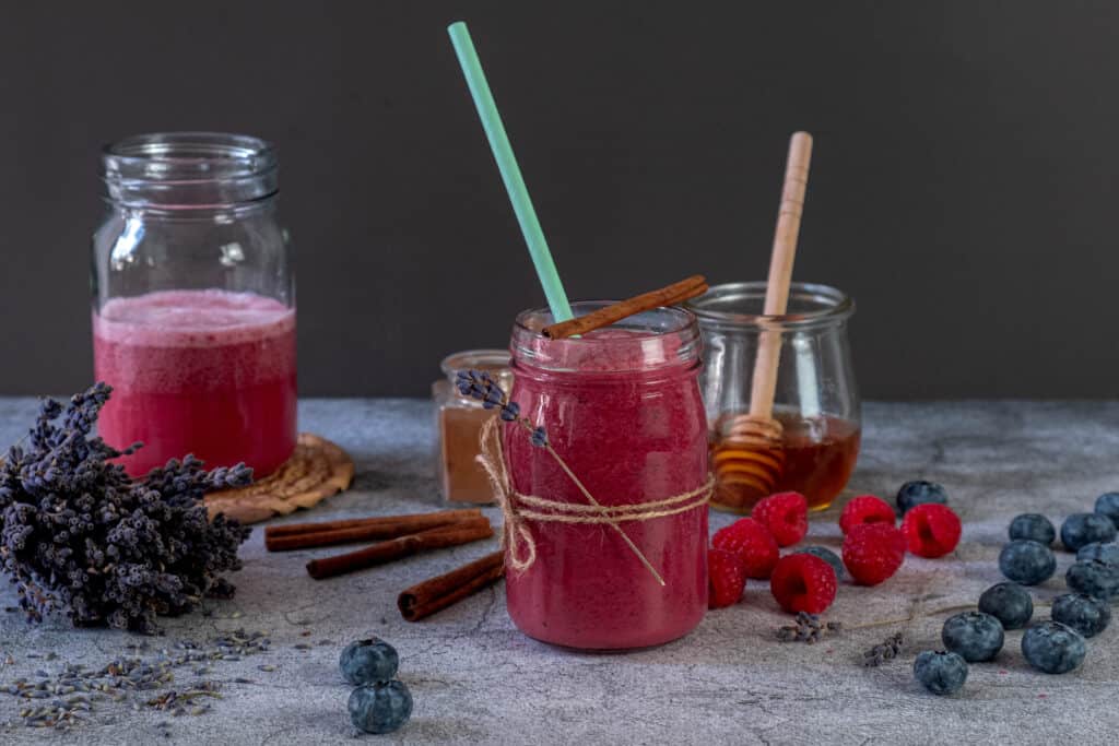 glass of blueberry and raspberry smoothie with ingredients surrounding