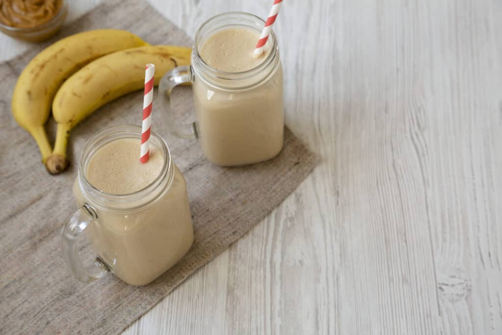 Peanut butter banana smoothie in glass jars on a white wooden background