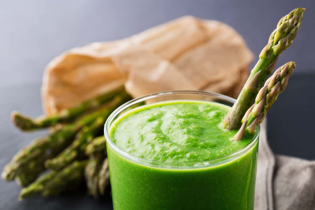 green asparagus smoothie in glass with asparagus in background