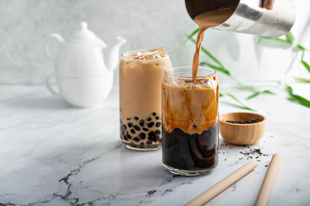 pouring coffee milk tea into two glasses with boba pearls