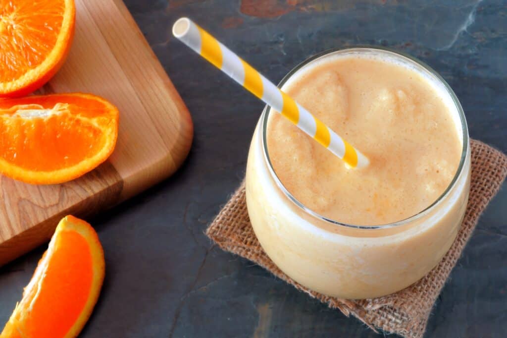 glass of orange juice smoothie on table with orange slices