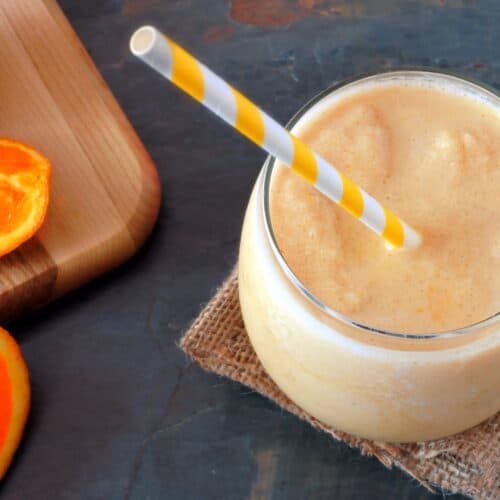 glass of orange juice smoothie on table with orange slices